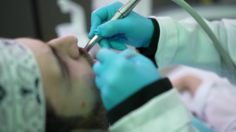 استخدام المعدات اللازمة لجراحة الفم, معالجة النخور وتركيب الحشوات،الزيارة الدورية للاطمئنان على الصحة الفموية، تصوير مقرب من الجانب لطبيبة ترتدي القفازات تقوم بفحص أسنان المريض وتشخيص المرض، شاب عربي خليجي عماني يرتدي الدشداشة والكمة يجلس على كرسي العلاج في العيادة السنية