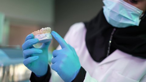 الاهتمام في الصحة الفموية ،  تقديم نصائح للمحافظة على صحة الفم والأسنان، مفهوم الطب والرعاية الصحية, تصوير مقرب لرجل عربي خليجي عماني يرتدي الكمه يجلس على كرسي العلاج ، طبيبة أسنان ترتدي المعطف والقفازات الطبية تمسك بيدها نموذج سني