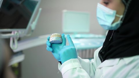 مفهوم الطب والرعاية الصحية, الاهتمام في الصحة الفموية ، تصوير مقرب لرجل عربي خليجي عماني يرتدي الكمه يجلس على كرسي العلاج ، طبيبة أسنان ترتدي المعطف والقفازات الطبية تمسك بيدها نموذج سني، تقديم نصائح للمحافظة على صحة الفم والأسنان