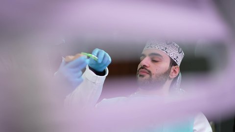 الاهتمام في الصحة الفموية, تقديم نصائح للمحافظة على صحة الفم والأسنان،مفهوم الطب والرعاية الصحية, ايماءات الاطمئنان والسرور، طبيبة أسنان ترتدي المعطف والقفازات الطبية تمسك بيدها نموذج سني، تصوير مقرب لرجل عربي خليجي عماني يرتدي الكمه يجلس على كرسي العلاج