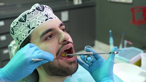 الاستعداد لحقن البنج الموضعي لتخفيف الشعور بالألم ,تقديم الرعاية الصحية في المراكز التخصصية، تصوير مقرب لرجل عربي خليجي عماني يرتدي الزي التقليدي يجلس في العيادة السنية بإيماءات السرور, يد طبيب أسنان يرتدي القفازات الطبية يمسك بيده إبرة المخدر،معالجة النخور والتسوس