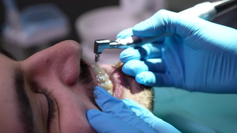 مفهوم الطب والرعاية الصحية، تصوير مقرب من الجانب لطبيب يرتدي القفازات يقوم بفحص أسنان المريض، شاب عربي خليجي عماني يرتدي الدشداشة والكمة يجلس على كرسي العلاج في العيادة السنية، إجراء الفحوصات الدورية للعناية بالصحة الفموية، تقديم الخدمات الطبية للمرضى