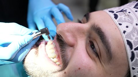 إجراء الفحوصات الدورية للعناية بالصحة الفموية، تقديم الخدمات الطبية للمرضى,مفهوم الطب والرعاية الصحية، تصوير مقرب من الجانب لطبيب يرتدي القفازات يقوم بفحص أسنان المريض، شاب عربي خليجي عماني يرتدي الدشداشة والكمة يجلس على كرسي العلاج في العيادة السنية