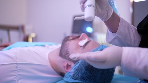 مفهوم العناية والإهتمام بنضارة وتحسين البشرة، ترطيب وتنظيف وتفتيح الجلد، رجل عربي خليجي عماني يرتدي الدشداشة يجلس على كرسي العيادة ، طبيبة مختصه فى العناية بالبشرة تضع كريم المرطب على وجه الزبون ، استخدام مكونات تجميلية شبابية