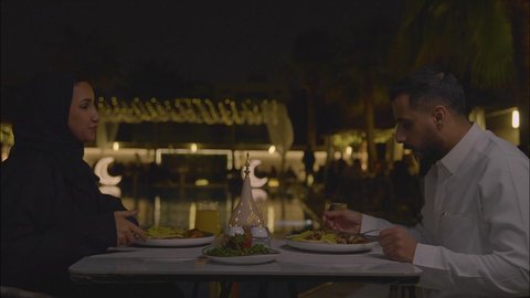 Enjoying a meal, a Saudi Arabian Gulf couple sitting in a restaurant, conversations and discussions at the dining table, the concept of a happy family, having a good time, a weekend get-together, getting to know each other and building social relationships, a table filled with Arabic food.