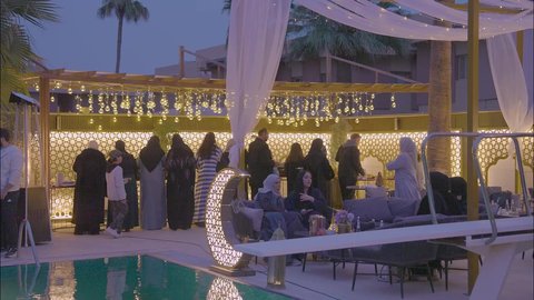 صالة مطعم ومقهى بديكورات وألوان جذابة، تصوير لمجموعه من الرجال والنساء السعوديين مجتمعين حول طاولة البوفيه المفتوح في العشاء ،أثاث داخلي راقي لمطعم على الطراز الحديث في المملكة العربية السعودية، الديكورات والتصاميم الداخلية للكافيهات والمطاعم