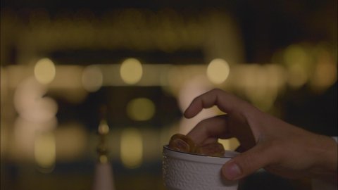 كرم الضيافة وحسن الاستقبال في شهر رمضان المبارك، وجبة الرطب الصحية ذات القيمة الغذائية العالية, محصول زراعي محلي وطني سعودي، تصوير مقرب ليد رجل عربي خليجي سعودي يرتدي الثوب التقليدي يقدم وعاء مليء بحبات التمر الطازجة لزوجته باحدي شاليهات المملكه العربية السعودية