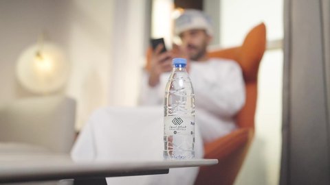 أهمية شرب الماء النقي للمحافظة على بشرة نضرة، الحفاظ على صحة الكلى ومعالجتها، التخلص من سموم الجسم،تصوير مقرب ليد رجل عربي خليجي عماني يرتدي الدشداشه والكمه  يقوم بشرب الماء م قارورة بلاستيكية ، ويمسك بيده الجوال ،المحافظة على سلامة الجهاز المناعي