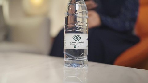 أهمية شرب الماء النقي للمحافظة على بشرة نضرة، المحافظة على سلامة الجهاز المناعي، التخلص من سموم الجسم، الحفاظ على صحة الكلى ومعالجتها، سيدة عربية خليجية سعودية ترتدي العباءه والحجاب تقوم بشرب الماء م قارورة بلاستيكية ، وتمسك بيدها الجوال ، دمج التقنيات المطورة فى الحياه اليوميه