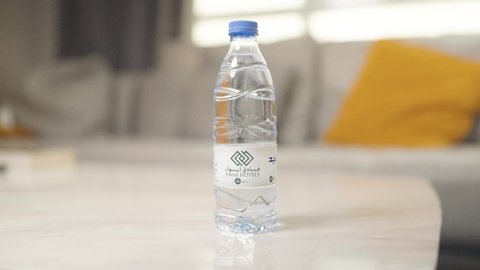 The importance of drinking pure water to maintain healthy skin, maintain and treat kidney health, maintain a healthy immune system, and detoxify the body. A close-up of a Saudi Arabian Gulf woman wearing an abaya and hijab drinking water from a plastic bottle.