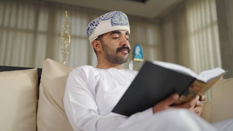 ممارسة الهوايات المفضلة،  تنمية المهارات الفكرية ، الاهتمام بالعلم والثقافة والدين ، تعزيز مفهوم المعرفة ،  قضاء الوقت بالمطالعة ،رجل عربي خليجي عماني يرتدي الدشداشه والكمه يجلس على كرسي مريح فى غرفة فندقيه ويقرأ كتاب ،  الاستمتاع بالهدوء والراحة داخل المنزل