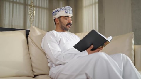 الاهتمام بالعلم والثقافة والدين ، تعزيز مفهوم المعرفة ، ممارسة الهوايات المفضلة،  تنمية المهارات الفكرية ،  قضاء الوقت بالمطالعة ،رجل عربي خليجي عماني يرتدي الدشداشه والكمه يجلس على كرسي مريح فى غرفة فندقيه ويقرأ كتاب ،  الاستمتاع بالهدوء والراحة داخل المنزل