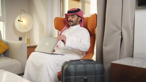ادارة الأعمال عن بعد، إنجاز المهام المطلوبة عبر اللابتوب، التطور والتكنولوجيا الحديثة، رجل عربي خليجي سعودي يرتدي الزى التقليدي مع الشماغ يجلس على كرسي مريح في غرفة فندقيه ويستخدم جهاز الحاسوب المحمول ، دمج التقنيات المتطوره فى الحياه اليوميه ، استخدام جهاز اللابتوب ، وظائف ومهن سعودية