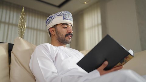 تعزيز مفهوم المعرفة ، الاهتمام بالعلم والثقافة والدين ، ممارسة الهوايات المفضلة،  تنمية المهارات الفكرية ،  قضاء الوقت بالمطالعة ،رجل عربي خليجي عماني يرتدي الدشداشه والكمه يجلس على كرسي مريح فى غرفة فندقيه ويقرأ كتاب ،  الاستمتاع بالهدوء والراحة داخل المنزل
