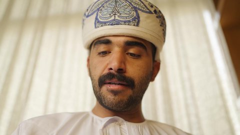 تنمية المهارات الفكرية ، الاهتمام بالعلم والثقافة والدين ، ممارسة الهوايات المفضلة،  قضاء الوقت بالمطالعة ،تعزيز مفهوم المعرفة ، تصوير مقرب لرجل عربي خليجي عماني يرتدي الدشداشه والكمه يقف بجانب مكتبه خشبيه ويقرأ كتاب ،  الاستمتاع بالهدوء والراحة داخل المنزل