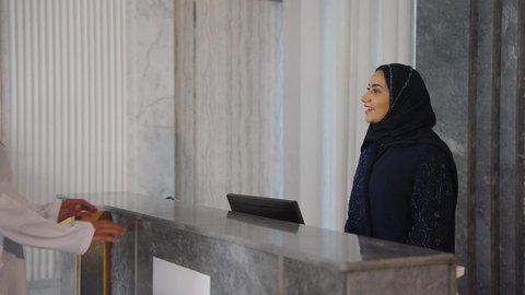 An Omani Gulf Arab family inquiring about customer service. An Omani Gulf Arab woman works in information, completing reservation and check-in procedures at the hotel reception desk. Tourism, hotels, and travel.