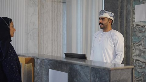 اتمام إجراءات الحجز والدخول لدى مكتب استقبال العملاء في الفندق، رجل عربي خليجي عماني يعمل في مجال الإستعلامات ، سياحه وفندقه وسفر، سيده عربية خليجية عمانيه تقوم بالاستفسار فى خدمة العملاء