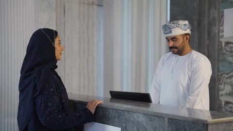 رجل عربي خليجي عماني يعمل في مجال الإستعلامات ، إجراءات الحجز والدخول لدى مكتب الاستقبال في الفندق، سياحه وفندقه وسفر، سيده عربية خليجية عمانيه تقوم بالاستفسار فى خدمة العملاء