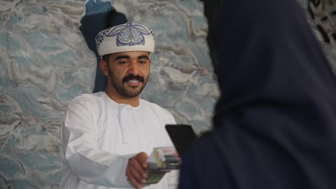 إجراءات الحجز والدخول لدى مكتب الاستقبال في الفندق، سياحه وفندقه وسفر،  رجل عربي خليجي عماني يقوم بالدفع عند الكاشير بطريقة الكترونية بإستخدام بطاقة الإئتمان البنكية، سيده عربية خليجية عمانيه ترتدي العباءه والحجاب تعمل في مجال الإستعلامات ،إستعلامات وإستفسارات فى خدمة العملاء