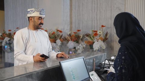 إستلام بطاقة الغرفة ، إجراءات الحجز والدخول لدى مكتب الاستقبال في الفندق،  سيده عربيه خليجيه عمانيه ترتدي العباءه والحجاب  تعطي كرت المفتاح لنزيل عماني في الفندق السياحي ،إستعلامات وإستفسارات فى خدمة العملاء