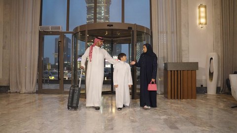 Spending quality time with family, enjoying the summer vacation, a Saudi Arabian Gulf family dragging a suitcase near the hotel reception desk, tourism, hotels, and travel