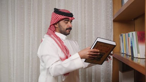 قضاء الوقت بالمطالعة ، ممارسة الهوايات المفضلة، تنمية المهارات الفكرية ، الاهتمام بالعلم والثقافة والدين ، تعزيز مفهوم المعرفة ، رجل عربي خليجي سعودي يرتدي الزى التقليدي مع الشماغ يقف بجانب مكتبه خشبيه ، يأخذ منها كتاب ويبدأ بالقراءه ،  الاستمتاع بالهدوء والراحة داخل المنزل