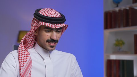 ادارة الأعمال عن بعد، التطور والتكنولوجيا الحديثة، وظائف ومهن سعودية، دمج التقنيات المتطوره فى الحياه اليوميه ، إنجاز المهام المطلوبة عبر اللابتوب، تصوير مقرب لرجل عربي خليجي سعودي يرتدي الزى التقليدي مع الشماغ يجلس على كرسي في غرفة المعيشه ويستخدم جهاز الحاسوب المحمول