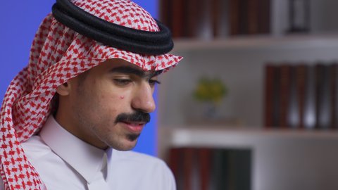 دمج التقنيات المتطوره فى الحياه اليوميه ، إنجاز المهام المطلوبة عبر اللابتوب، ادارة الأعمال عن بعد، التطور والتكنولوجيا الحديثة،تصوير مقرب لرجل عربي خليجي سعودي يرتدي الزى التقليدي مع الشماغ يجلس على كرسي في غرفة المعيشه ويستخدم جهاز الحاسوب المحمول ، وظائف ومهن سعودية