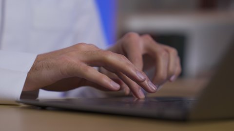 A close-up of a Saudi Arabian Gulf man wearing traditional clothing and a shemagh sitting on a chair in the living room using a laptop. This image highlights developments and modern technology, remote business management, laptop use, integrating advanced technologies into daily life, and completing tasks via laptop.