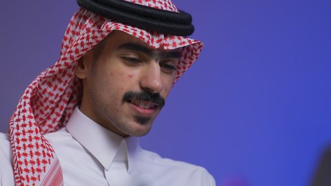 ادارة الأعمال عن بعد، التطور والتكنولوجيا الحديثة،تصوير مقرب لرجل عربي خليجي سعودي يرتدي الزى التقليدي مع الشماغ يجلس على كرسي في غرفة المعيشه ويستخدم جهاز الحاسوب المحمول ، وظائف ومهن سعودية،  دمج التقنيات المتطوره فى الحياه اليوميه ، إنجاز المهام المطلوبة عبر اللابتوب، استخدام جهاز اللابتوب