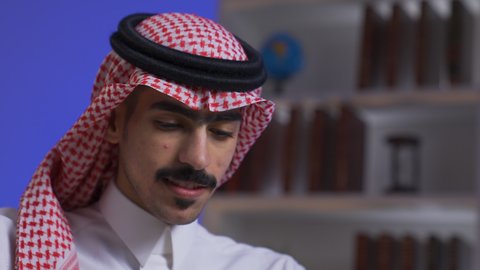 ادارة الأعمال عن بعد، التطور والتكنولوجيا الحديثة، وظائف ومهن سعودية،  دمج التقنيات المتطوره فى الحياه اليوميه ، إنجاز المهام المطلوبة عبر اللابتوب، تصوير مقرب لرجل عربي خليجي سعودي يرتدي الزى التقليدي مع الشماغ يجلس على كرسي في غرفة المعيشه ويستخدم جهاز الحاسوب المحمول ، استخدام جهاز اللابتوب