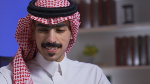 وظائف ومهن سعودية،  دمج التقنيات المتطوره فى الحياه اليوميه ، إنجاز المهام المطلوبة عبر اللابتوب، ادارة الأعمال عن بعد، التطور والتكنولوجيا الحديثة، تصوير مقرب لرجل عربي خليجي سعودي يرتدي الزى التقليدي مع الشماغ يجلس على كرسي في غرفة المعيشه ويستخدم جهاز الحاسوب المحمول ، استخدام جهاز اللابتوب