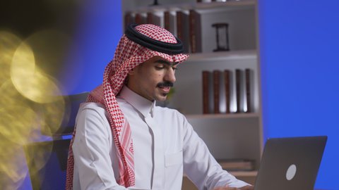 ادارة الأعمال عن بعد، التطور والتكنولوجيا الحديثة،  دمج التقنيات المتطوره فى الحياه اليوميه ، إنجاز المهام المطلوبة عبر اللابتوب، وظائف ومهن سعودية، رجل عربي خليجي سعودي يرتدي الزى التقليدي مع الشماغ يجلس على كرسي في غرفة المعيشه ويستخدم جهاز الحاسوب المحمول ، استخدام جهاز اللابتوب