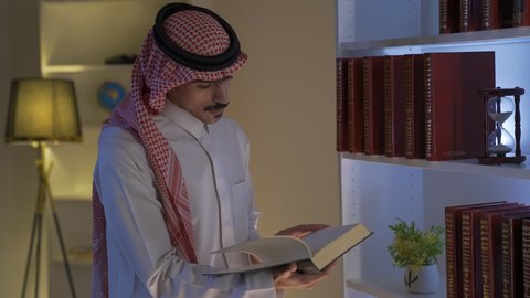 الاستمتاع بالهدوء والراحة داخل المنزل، ممارسة الهوايات المفضلة، تصوير لرجل عربي خليجي سعودي يرتدي الزى التقليدي مع الشماغ يجلس في غرفة المعيشة ويقوم بقراءة كتاب ،الاستمتاع بقراءة الروايات والقصص ، قضاء الوقت بالمطالعة ، تنمية المهارات الفكرية ،تعزيز مفهوم الثقافة والمعرفة