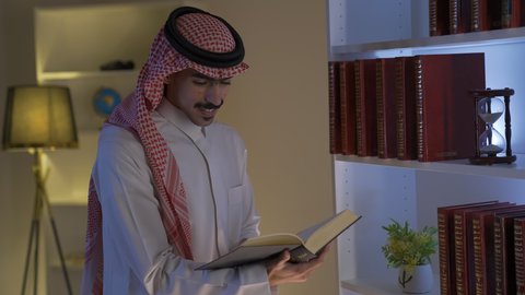 ممارسة الهوايات المفضلة، تصوير لرجل عربي خليجي سعودي يرتدي الزى التقليدي مع الشماغ يجلس في غرفة المعيشة ويقوم بقراءة كتاب ،الاستمتاع بقراءة الروايات والقصص ، قضاء الوقت بالمطالعة ، تنمية المهارات الفكرية ، الاستمتاع بالهدوء والراحة داخل المنزل، تعزيز مفهوم الثقافة والمعرفة