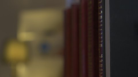 Enjoying peace and comfort at home, developing intellectual skills, enhancing the concept of culture and knowledge, practicing favorite hobbies, a picture of a Saudi Arabian Gulf man wearing traditional clothing with a shemagh taking a book from the home library and reading it, enjoying reading novels and stories, spending time reading.