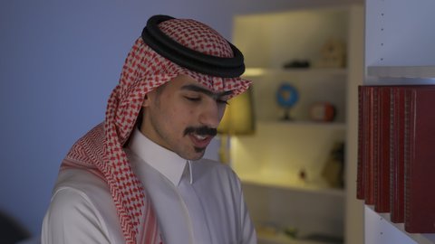 الاستمتاع بالهدوء والراحة داخل المنزل، ممارسة الهوايات المفضلة، الاستمتاع بقراءة الروايات والقصص ،تنمية المهارات الفكرية ، تصوير من الجانب لرجل عربي خليجي سعودي يرتدي الزى التقليدي مع الشماغ يجلس على الأريكة في غرفة المعيشة ويقوم بقراءة كتاب ،قضاء الوقت بالمطالعة والثقافة،  تعزيز مفهوم الثقافة والمعرفة