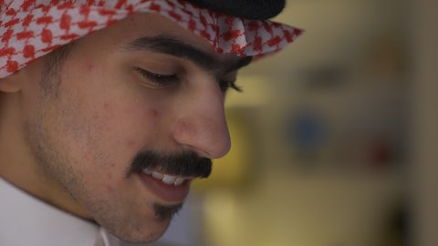 Practicing favorite hobbies, enjoying peace and comfort at home, developing intellectual skills, a close-up of a Saudi Arabian Gulf man wearing traditional clothing with a shemagh sitting on a sofa in the living room reading a book, spending time reading and cultivating knowledge, enjoying novels and stories, promoting the concept of culture and knowledge.