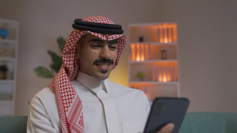 اجراء مكالمه فيديو ،التواصل مع العملاء عن بعد، تصفح وسائل التواصل الاجتماعي ، استخدام التقنيات الحديثة و المتطورة في العمل, إجراء اتصال هاتفي عبر الجوال, مهن و أعمال في السعودية, شاب عربي خليجي سعودي يرتدي الثوب التقليدي و الشماغ  يمسك الهاتف المحمول بيده