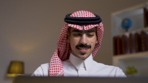 إنجاز المهام المطلوبة عبر اللابتوب، دمج التقنيات المتطوره فى الحياه اليوميه ، وظائف ومهن سعودية، ادارة الأعمال عن بعد، التطور والتكنولوجيا الحديثة، رجل عربي خليجي سعودي يرتدي الزى التقليدي مع الشماغ يجلس على كرسي في غرفة المعيشه ويستخدم جهاز الحاسوب المحمول ، استخدام جهاز اللابتوب