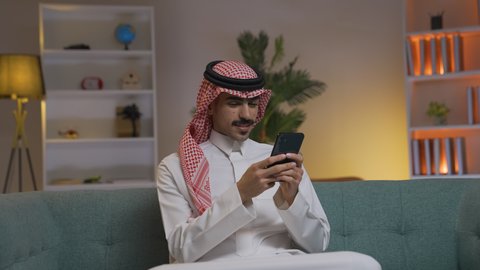 الاطمئنان على الاهل والاصدقاء، شاب عربي خليجي سعودي يرتدي الثوب التقليدي و الشماغ يمسك الهاتف المحمول بيده، التواصل مع العملاء عن بعد،  تصفح وسائل التواصل الاجتماعي ،إجراء اتصال هاتفي عبر الجوال, مهن و أعمال في السعودية, استخدام التقنيات الحديثة و المتطورة في العمل, الدردشه عبر الانترنت