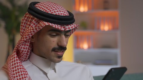 إجراء اتصال هاتفي عبر الجوال, مهن و أعمال في السعودية, التواصل مع العملاء عن بعد،تصفح وسائل التواصل الاجتماعي ،استخدام التقنيات الحديثة و المتطورة في العمل, الدردشه عبر الانترنت، شاب عربي خليجي سعودي يرتدي الثوب التقليدي و الشماغ يمسك الهاتف المحمول بيده