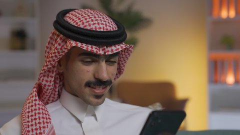 التواصل مع العملاء عن بعد،تصفح وسائل التواصل الاجتماعي ،استخدام التقنيات الحديثة و المتطورة في العمل, الدردشه عبر الانترنت، إجراء اتصال هاتفي عبر الجوال, مهن و أعمال في السعودية, شاب عربي خليجي سعودي يرتدي الثوب التقليدي و الشماغ يمسك الهاتف المحمول بيده