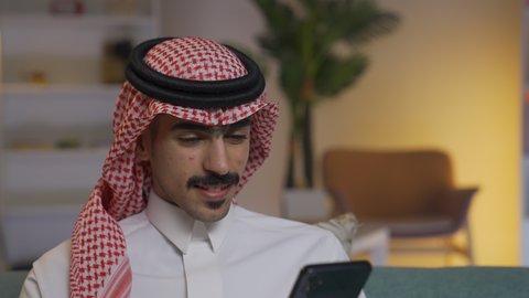 استخدام التقنيات الحديثة و المتطورة في العمل, الدردشه عبر الانترنت، إجراء اتصال هاتفي عبر الجوال, مهن و أعمال في السعودية, شاب عربي خليجي سعودي يرتدي الثوب التقليدي و الشماغ يمسك الهاتف المحمول بيده, التواصل مع العملاء عن بعد،تصفح وسائل التواصل الاجتماعي