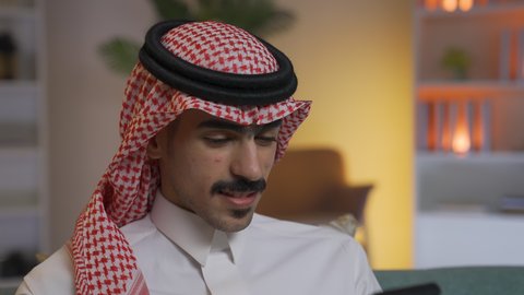 Chatting online, making a phone call via mobile, using modern and advanced technologies at work, professions and businesses in Saudi Arabia, a young Saudi Arabian Gulf man wearing traditional thobe and shemagh holding a mobile phone in his hand, communicating with clients remotely, browsing social media