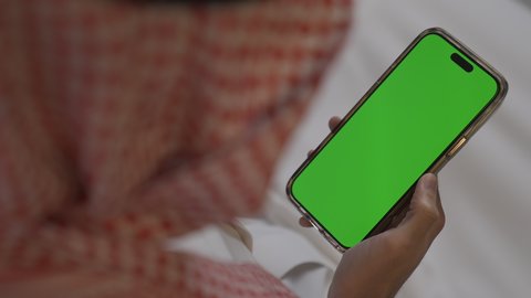 دمج التقنيات المتطورة في الحياه اليوميه , تصفح وسائل التواصل الاجتماعي ،عرض شاشه خضراء كروما فارغه، شاب عربي خليجي سعودي يرتدي الثوب التقليدي و الشماغ يمسك الهاتف المحمول بيده، إجراء اتصال هاتفي عبر الجوال, مهن و أعمال في السعودية, الدردشه عبر الانترنت