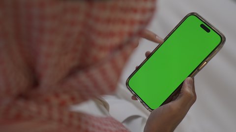 تصفح وسائل التواصل الاجتماعي ،عرض شاشه خضراء كروما فارغه، شاب عربي خليجي سعودي يرتدي الثوب التقليدي و الشماغ يمسك الهاتف المحمول بيده، إجراء اتصال هاتفي عبر الجوال, مهن و أعمال في السعودية, استخدام التقنيات الحديثة و المتطورة في العمل, الدردشه عبر الانترنت
