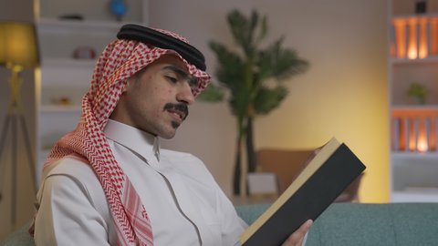 ممارسة الهوايات المفضلة، الاستمتاع بالهدوء والراحة داخل المنزل، تنمية المهارات الفكرية ، قضاء الوقت بالمطالعة والثقافة،  تصوير من الجانب لرجل عربي خليجي سعودي يرتدي الزى التقليدي مع الشماغ يجلس على الأريكة في غرفة المعيشة ويقوم بقراءة كتاب ، الاستمتاع بقراءة الروايات والقصص ، تعزيز مفهوم الثقافة والمعرفة
