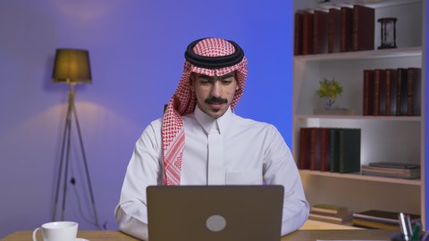 ادارة الأعمال عن بعد، إنجاز المهام المطلوبة عبر اللابتوب، التطور والتكنولوجيا الحديثة، رجل عربي خليجي سعودي يرتدي الزى التقليدي مع الشماغ يجلس على كرسي في غرفة المعيشه ويستخدم جهاز الحاسوب المحمول ، دمج التقنيات المتطوره فى الحياه اليوميه ، استخدام جهاز اللابتوب ، وظائف ومهن سعودية