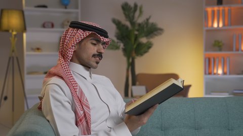 الاستمتاع بقراءة الروايات والقصص ، تعزيز مفهوم الثقافة والمعرفة ، تنمية المهارات الفكرية ، الاستمتاع بالهدوء والراحة داخل المنزل، قضاء الوقت بالمطالعة والثقافة، ممارسة الهوايات المفضلة،رجل عربي خليجي سعودي يرتدي الزى التقليدي مع الشماغ يجلس على الأريكة في غرفة المعيشة ويقوم بقراءة كتاب